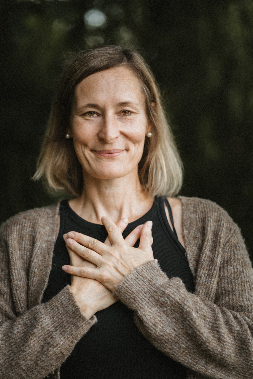 Katrin Rick mit den Händen auf dem Herzen, Porträt vor dunklem Hintergrund